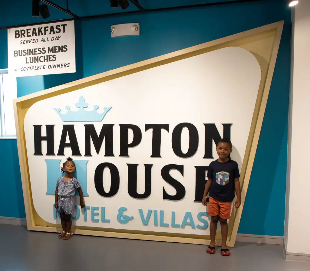 two children standing in front of a large sign that reads "Hampton House Hotel and Villas"