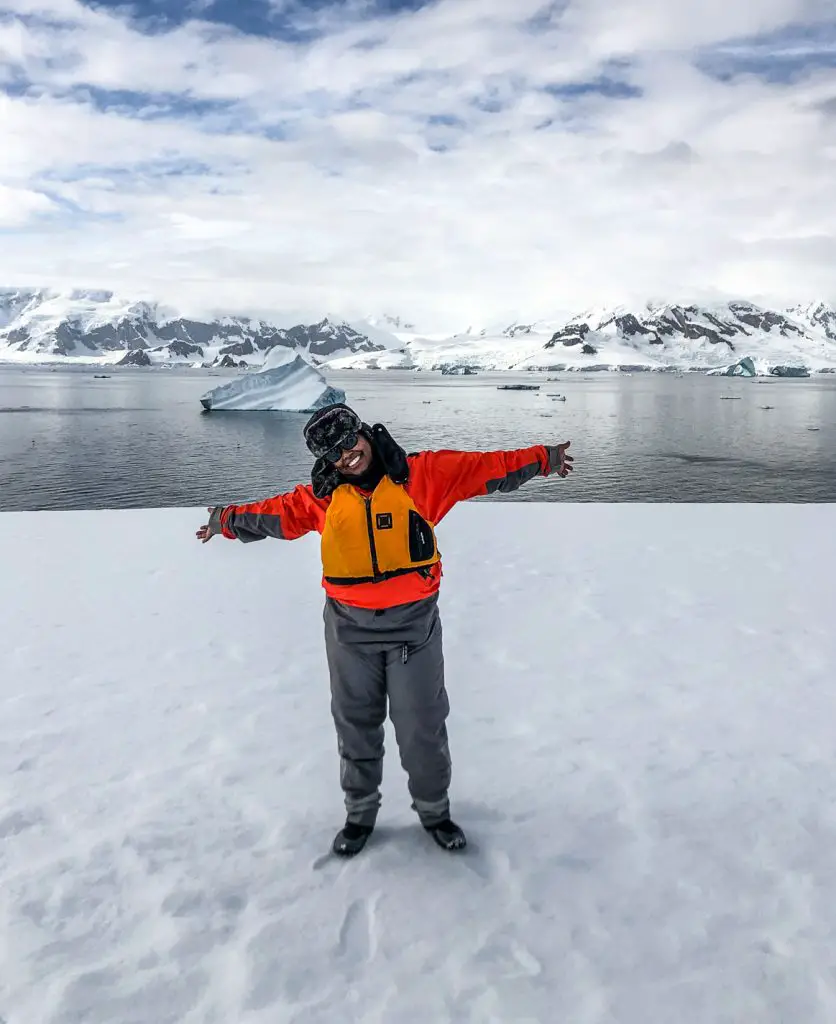 Woman standing on snowy hill with antarctica dark water behind her and behind that large snowcapped mountains