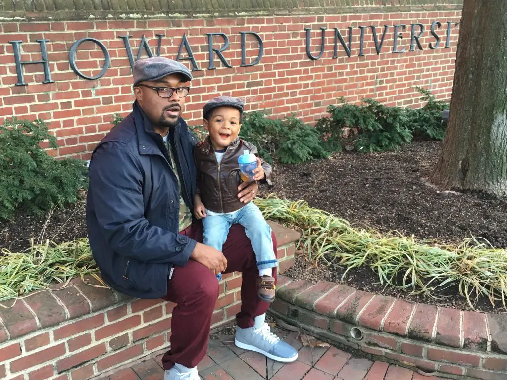 Man holding toddler while sitting in front of the Howard Univesity sign