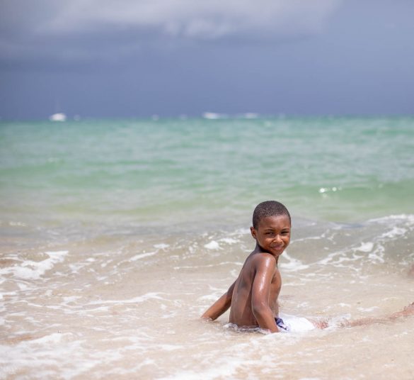 little boy in ocean water looking back as stormy clouds roll in