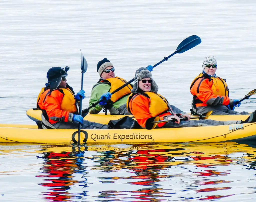 Black woman sitting in the back of a two-seat kayak with another couple of kayakers on the water.