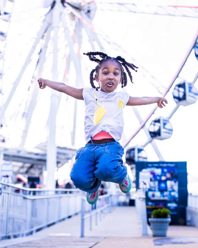 Little girl in midair jump in front of a Ferris Wheel