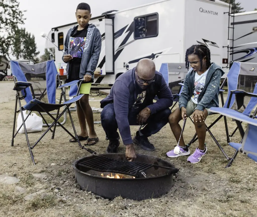 father stokes fire while and two kids wait with marshmallows on sticks