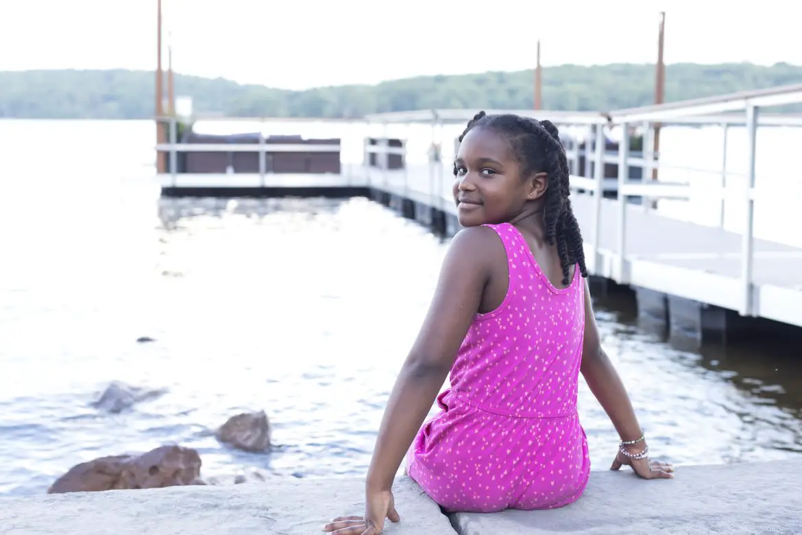 little girl sitting next to Deep creek lake in maryland smiling